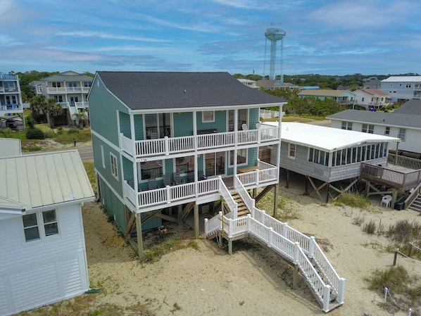 A multi-story beachfront house with a balcony, a staircase leading to the upper floor, and a sandy beach area. - Experience oceanfront living at the spacious 5-bedroom Pilot House in Oak Island, NC. (Oak Island)