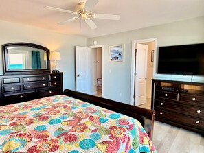 Een hotelkamer met een bed, een kaptafel, een televisie, een plafondventilator en een deur naar een andere kamer.