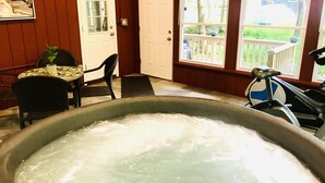 Ein Zimmer mit Whirlpool, Tisch mit Stühlen, einer Tür und Fenstern mit Blick ins Freie.
