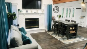 Ein Wohnzimmer mit Kamin, einem Essbereich mit Tisch und Stühlen sowie einem an der Wand montierten Fernseher.