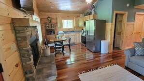 A cozy cabin interior with a stone fireplace, wooden dining table, and a gray sofa. - Beech View Haven- Custom Log Home in Hocking Hills (Logan)