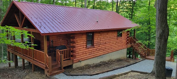 A log cabin with a metal roof, a porch, and a staircase leading to a deck. - Beech View Haven- Custom Log Home in Hocking Hills (Logan)