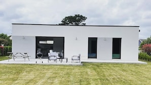 A modern, single-story house with a flat roof, a patio with outdoor furniture, and a large window. - New house near Port-Manec'h beach (Nevez)