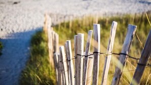 A wooden fence with barbed wire, leading to a beach with sand and water. - New house near Port-Manec'h beach (Nevez)