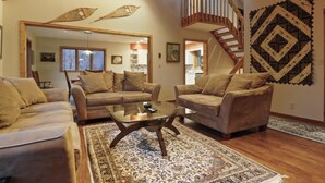 Un salon spacieux avec une grande fenêtre, un escalier en bois et un tapis à motifs.