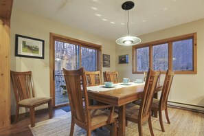 Une salle à manger avec une table et des chaises en bois, de grandes fenêtres et un luminaire suspendu.