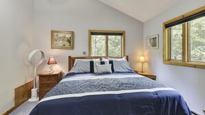Une chambre à coucher comprenant un lit, deux tables de chevet, une commode, un lampadaire et deux fenêtres avec des cadres en bois.
