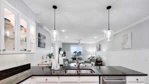 Une cuisine moderne avec des meubles blancs, un plan de travail en granit noir, un évier en acier inoxydable et des luminaires suspendus.