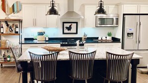 Una cocina moderna con armarios blancos, un microondas de acero inoxidable, un refrigerador y una isla central con taburetes de bar.