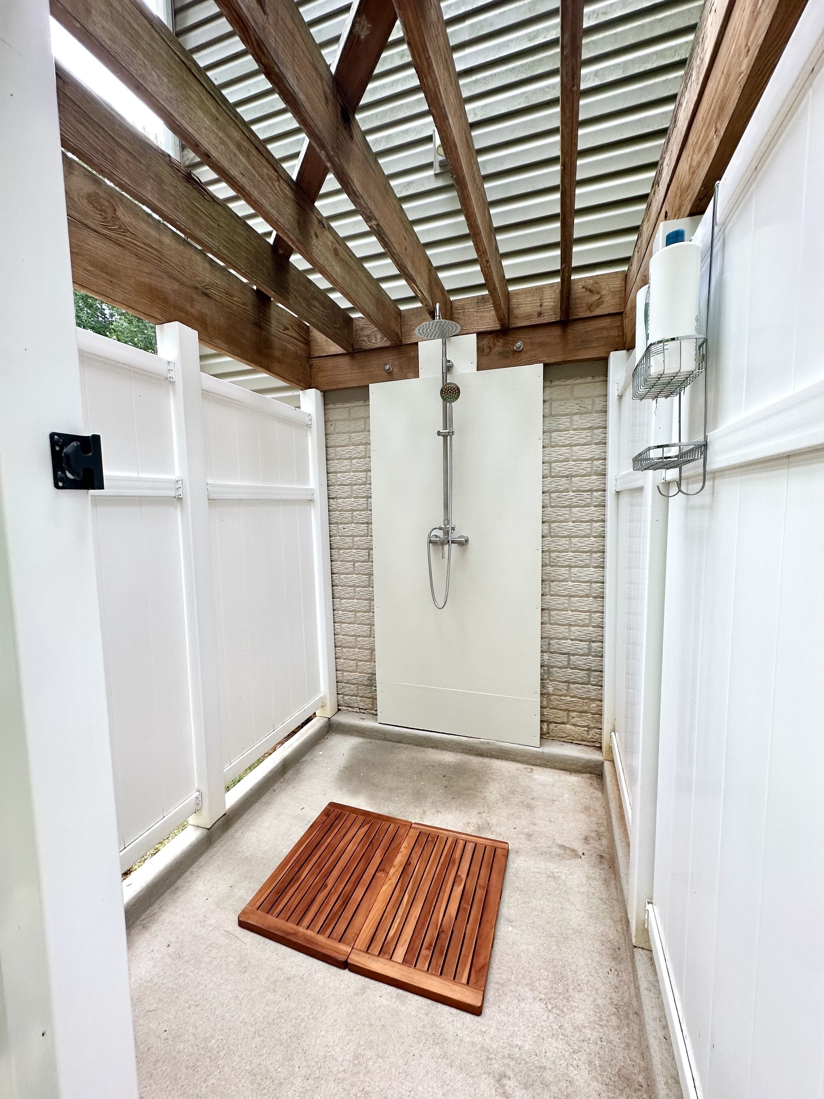 Ein überdachter Patio-Bereich mit Holzdeck, Dusche und Steinmauer.