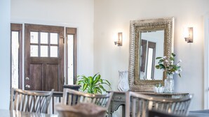 Un comedor con puerta de madera, un espejo grande y un jarrón con flores.
