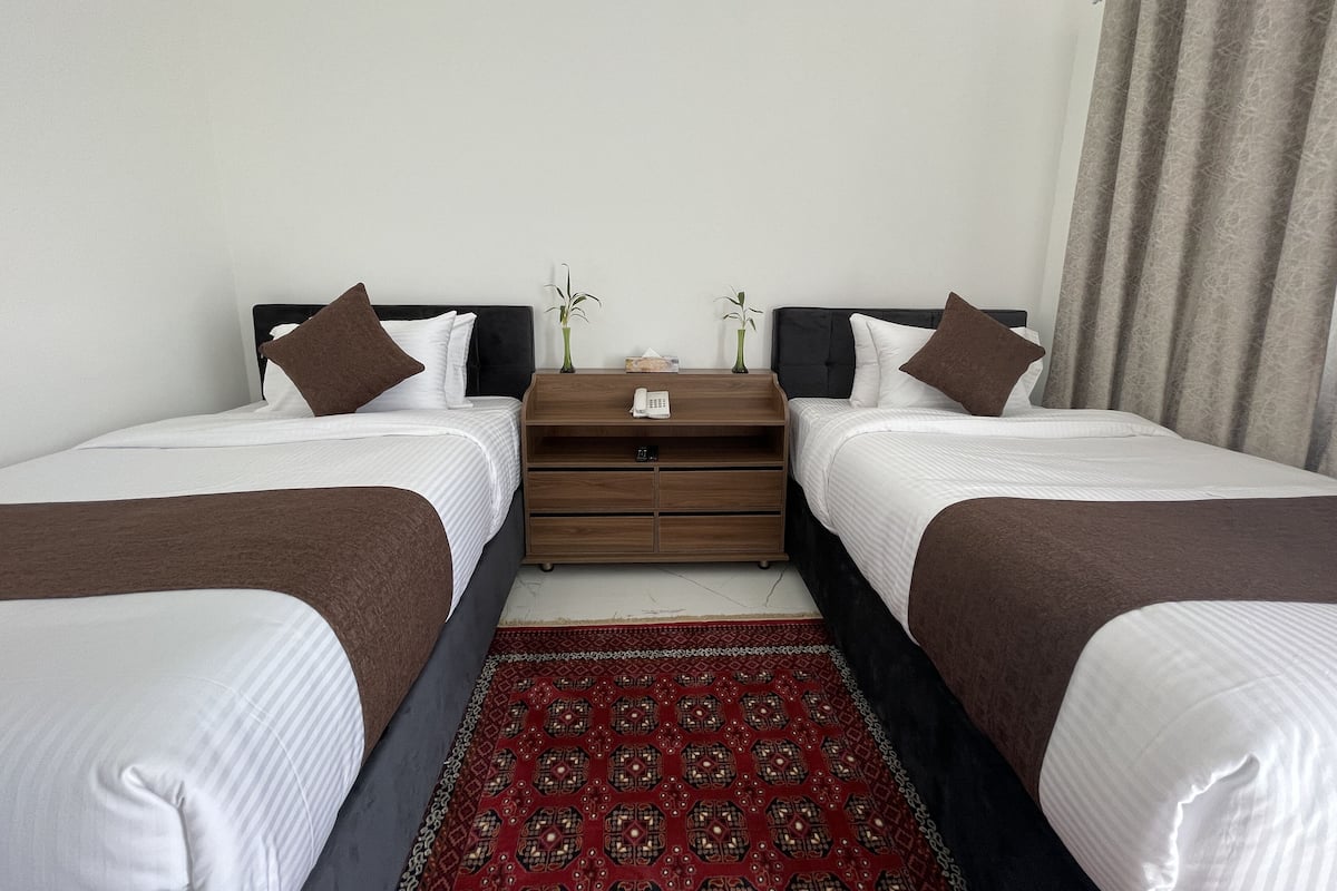A hotel room with two beds, a wooden nightstand, a telephone, and a red patterned rug.
