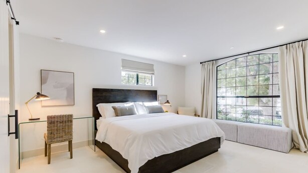 A modern bedroom with a large bed, a glass bench, a bedside table with a lamp, and a window with curtains. - Casa Valerio Unit 6C (Santa Barbara)