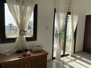 A room with a large window, a wooden dresser, a small white basket, and a potted plant.