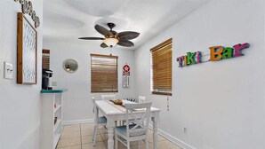 A dining area with a white table and chairs, a ceiling fan, and a wall sign reading 'Tiki Bar'. - The Funky Cactus House - Team Joseph Ellen (Jacksonville)