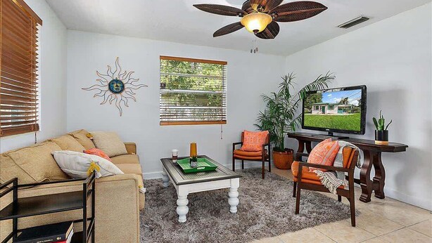 A living room with a ceiling fan, a television, a sofa, a coffee table, and a window with blinds. - The Funky Cactus House - Team Joseph Ellen (Jacksonville)
