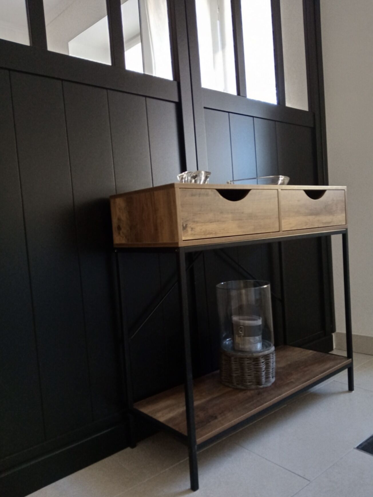 Une console en bois dotée de deux tiroirs et d’un récipient en verre, le tout posé sur un support en métal noir.