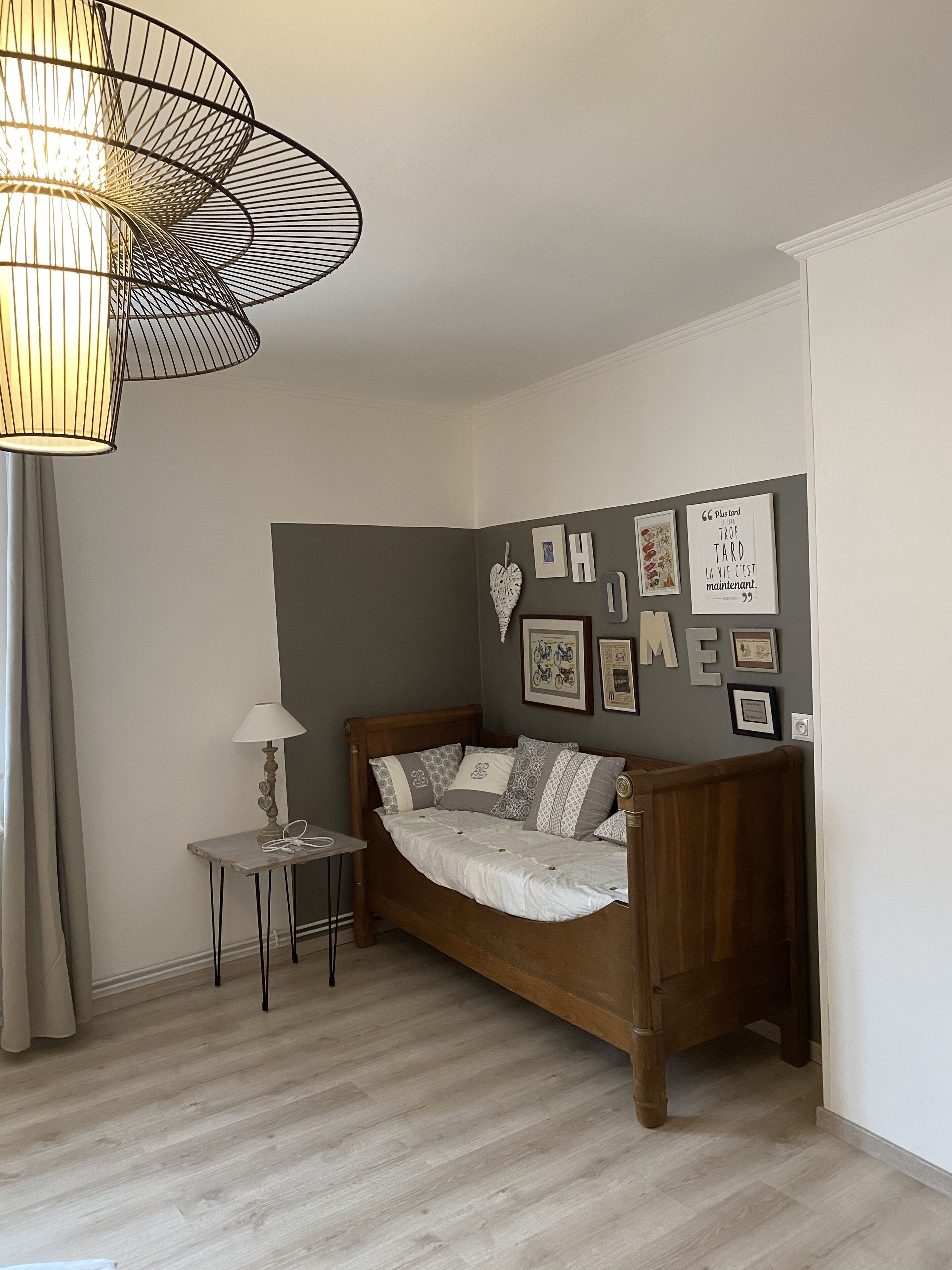 Un dormitorio con cama de madera, una mesita de noche pequeña, una lámpara y una pared decorada con marcos y una cita.