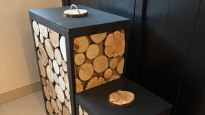 Kaksi mustaa sivupöytää, joiden designissä on käytetty puunrunkoaihetta, on sijoitettu laatoitetulle lattialle tumman seinän eteen.