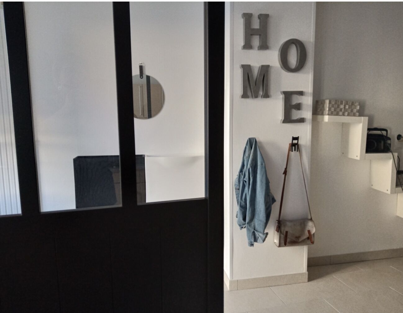 Et moderne interiør med et spejl med sort ramme, en denimjakke hængende på en knage, og ordet 'HOME' på væggen.