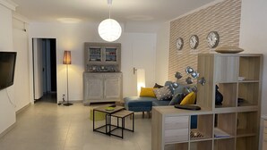 Moderni olohuone, jossa on litteänäyttöinen televisio, puinen kaappi, sininen sohva ja koristeellinen seinäkello.