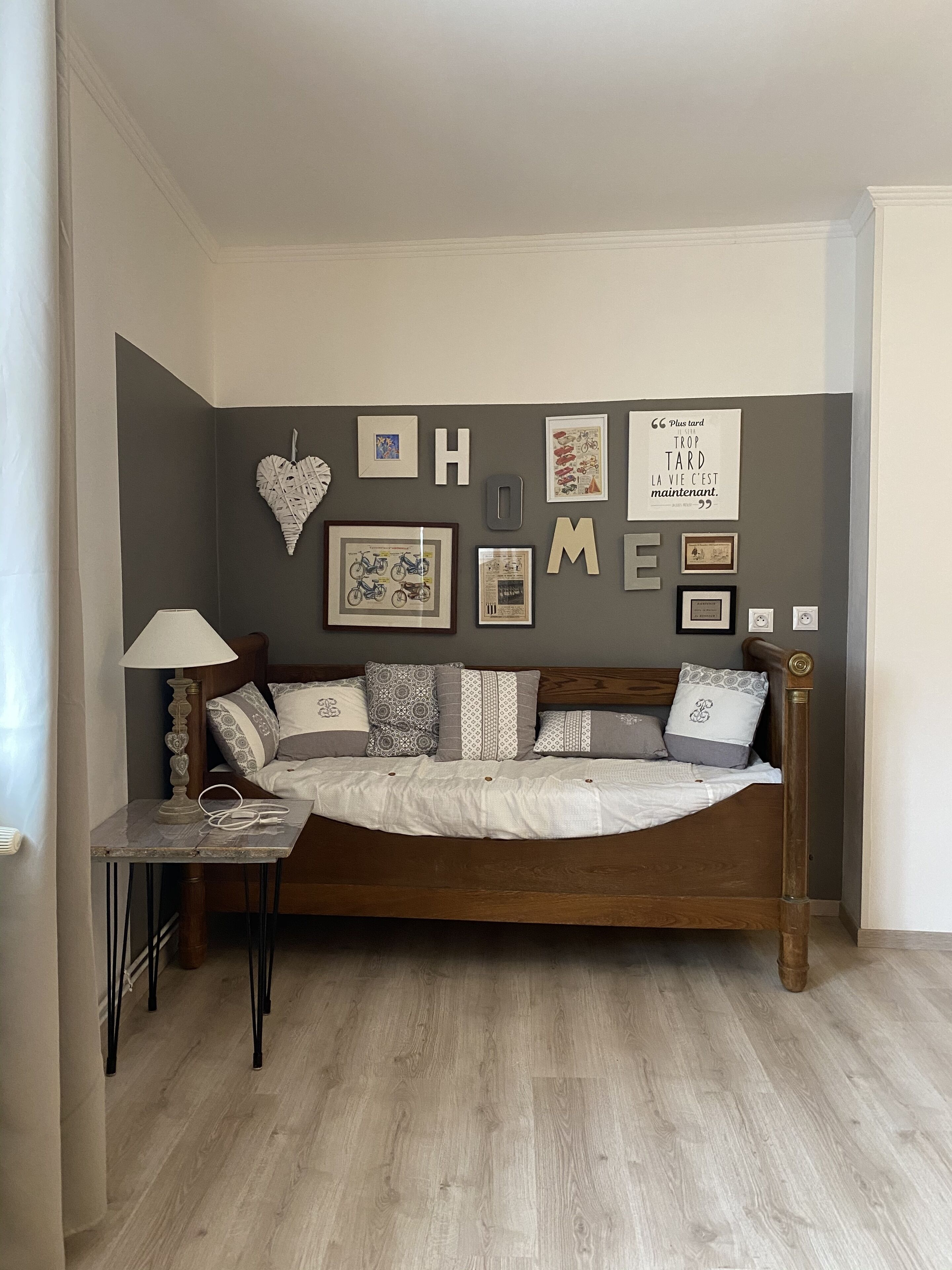 Une chambre confortable avec un lit en bois, une table de chevet avec une lampe et un mur décoré de tableaux encadrés et d’un ornement en forme de cœur.