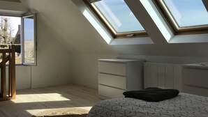 Ein Schlafzimmer mit Oberlichtern, einem Bett, einer Kommode und einem Sessel.