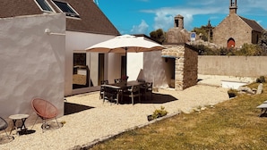 Ein modernes Haus mit Terrasse, einer Steinmauer und einer Kirche im Hintergrund.