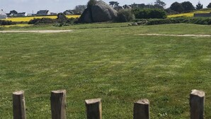 Ein grasbewachsenes Feld mit einer großen Felsformation in der Ferne, umgeben von einem Holzzaun.