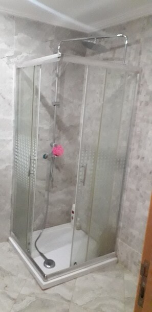 A glass-enclosed shower stall with a showerhead and a pink object hanging on the door.