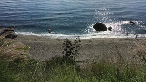Ein Strand mit einem Felsen im Wasser, Wellen, die auf das Ufer brechen, und einem klaren Himmel.