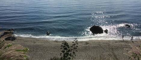 En strand med en klippformation som sträcker sig ut i vattnet, vågor som bryter mot stranden och en klar himmel.