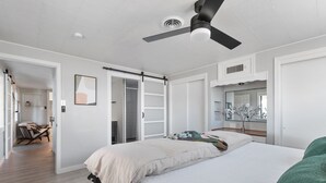 Un dormitorio con cama, ventilador de techo, armario y baño visible a través de una puerta abierta.