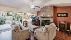 A living room with a fireplace, a television, and a large window overlooking a natural landscape. - 47MF - WiFi - Fireplace - Sleeps 6 3 Bedroom Home by RedAwning (Maple Falls)