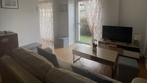 Un salon avec un canapé, une table basse, un téléviseur et une fenêtre avec des rideaux.