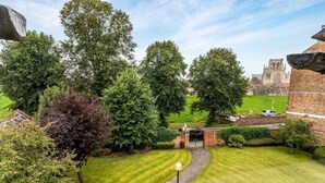 A well-maintained garden with a paved pathway leading to a gate, surrounded by mature trees and a brick building in the background. - 14 Feversham House · Stylish 1-Bed Apartment with York Minster Views - Pass The Keys (York)