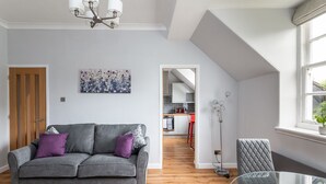 A modern living room with a grey sofa, a glass coffee table, and a red chair. A kitchen is visible in the background. - 14 Feversham House · Stylish 1-Bed Apartment with York Minster Views - Pass The Keys (York)