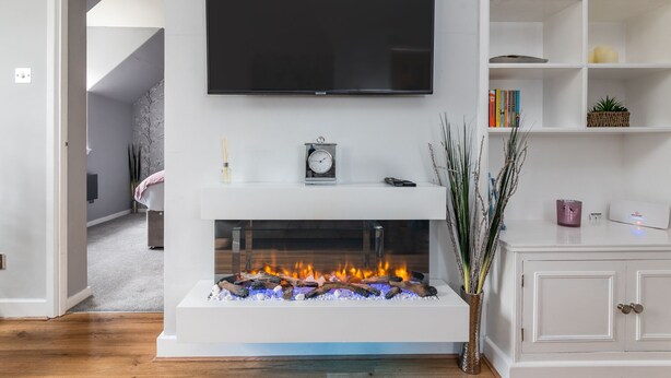 A modern living room with a flat-screen TV mounted above a fireplace, a bookshelf with books and decorative items, and a door leading to another room. - 14 Feversham House · Stylish 1-Bed Apartment with York Minster Views - Pass The Keys (York)