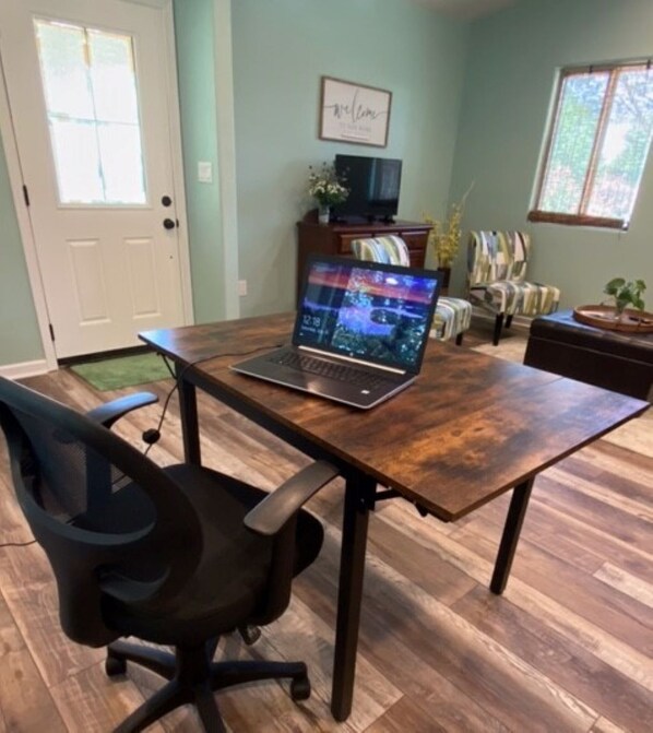 A room with a wooden table, a laptop, a black office chair, a bookshelf, and a window with a view of trees. - Private, Quite and Comfortable (Burleson)