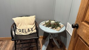 Puinen tuoli, jossa on päällä pehmuste, ja pehmusteessa lukee sana ”RELAX”. Tuolin vieressä on pieni pöytä, jonka päällä on kynttilä ja havunoksia.