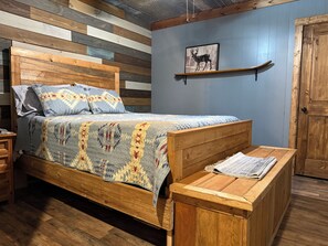 Ein Schlafzimmer mit einem hölzernen Bett, einer Bank, einem Regal mit einem Bild eines Rehs und einer Holztür.