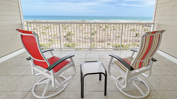Ein Balkon mit zwei Schaukelstühlen und einem kleinen Tisch, mit Blick auf einen Strand und eine Geländer.