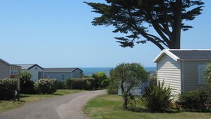 A rural road leading to a row of mobile homes with a large tree and a clear view of the sea. - Lovely mobile home in a 4-star residential estate in Les Sables D'Olonne (Les Sables-d'Olonne)