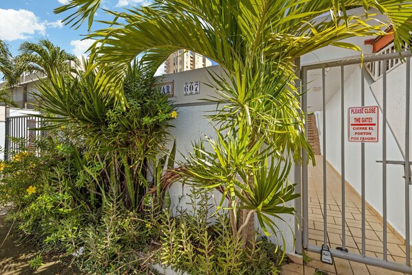 A gated entrance with a sign in multiple languages, surrounded by dense foliage and a clear sky.