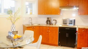 A modern kitchen with wooden cabinets, a glass dining table, and a coffee maker. - Burnaby Cozy suite Near Skytrain (Burnaby)