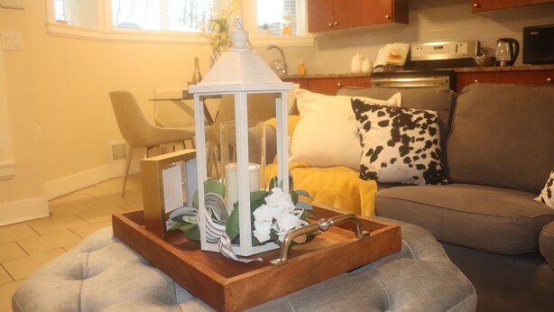 A living room with a grey sofa, a wooden side table, and a white lantern. - Burnaby Cozy suite Near Skytrain (Burnaby)