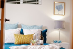 A neatly arranged bedroom with a bed, pillows, a bedside table with a lamp, a wine bottle, and a glass.