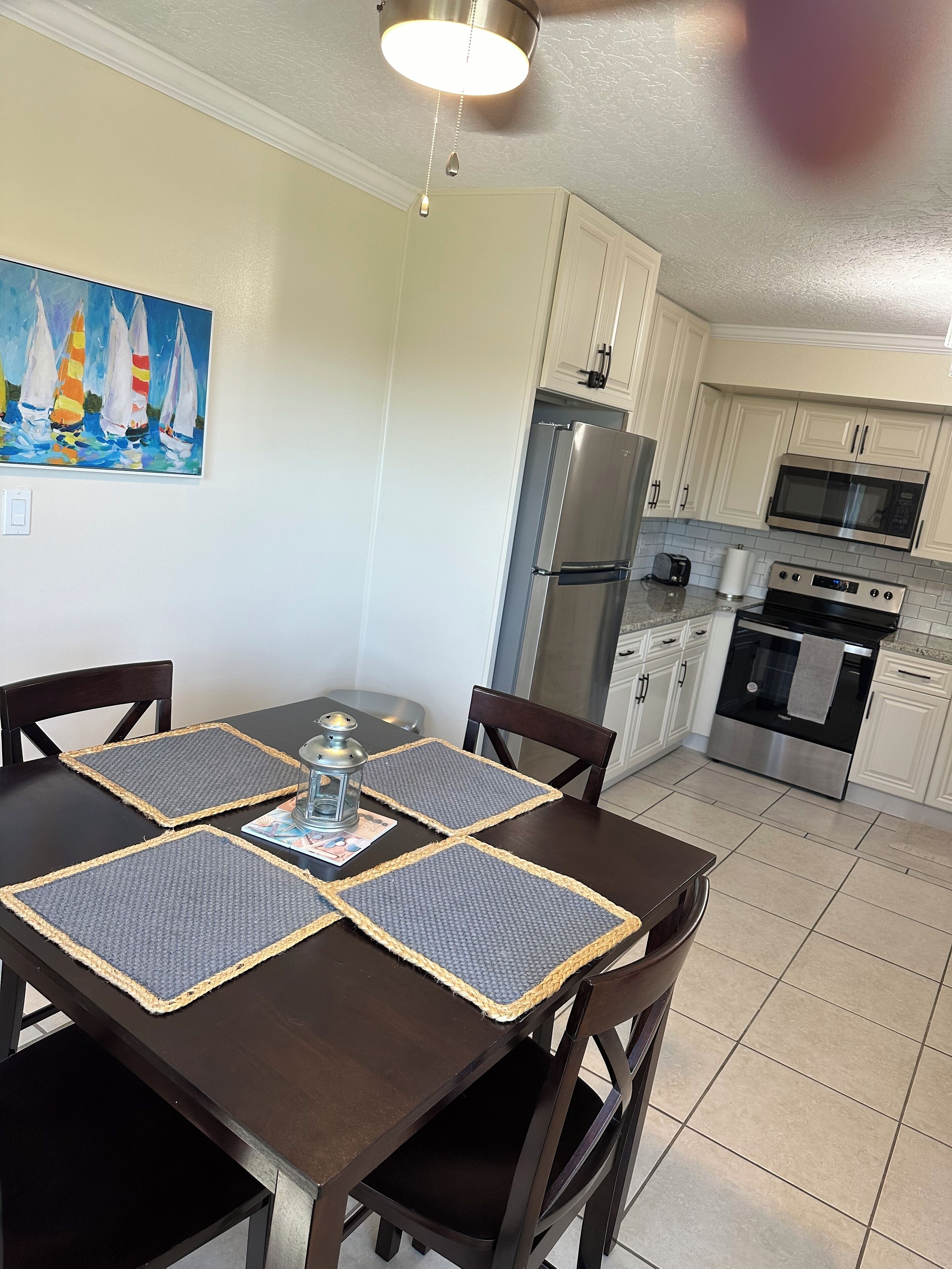 Una cocina moderna con armarios blancos, electrodomésticos de acero inoxidable y una zona de comedor con mesa y sillas de madera oscura.