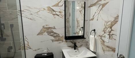 A bathroom with a glass shower enclosure, a black toilet, a white sink with a black cabinet, and a marble-patterned wall.