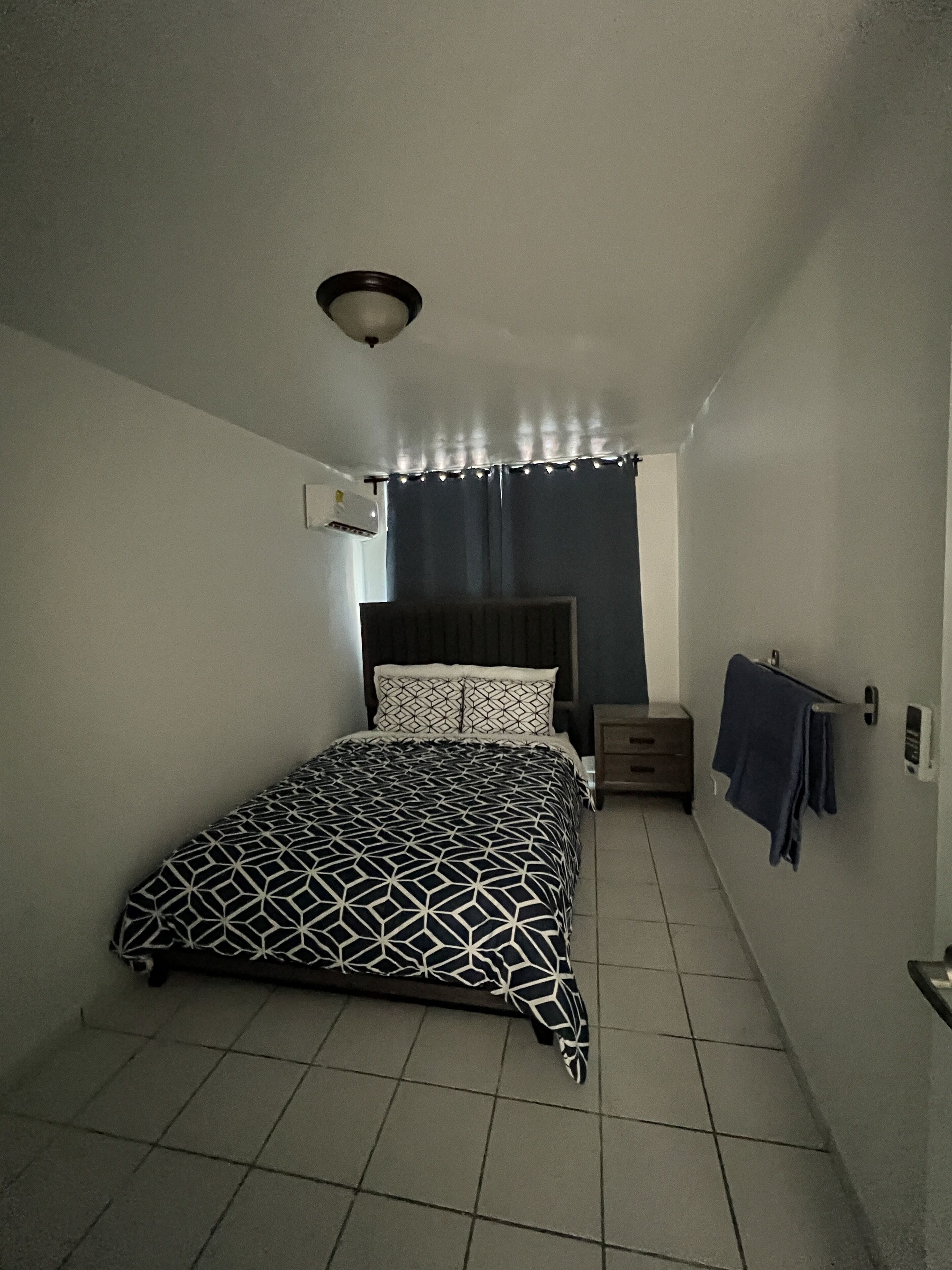 Une petite pièce étroite, avec un lit, une table de chevet et un porte-serviettes.